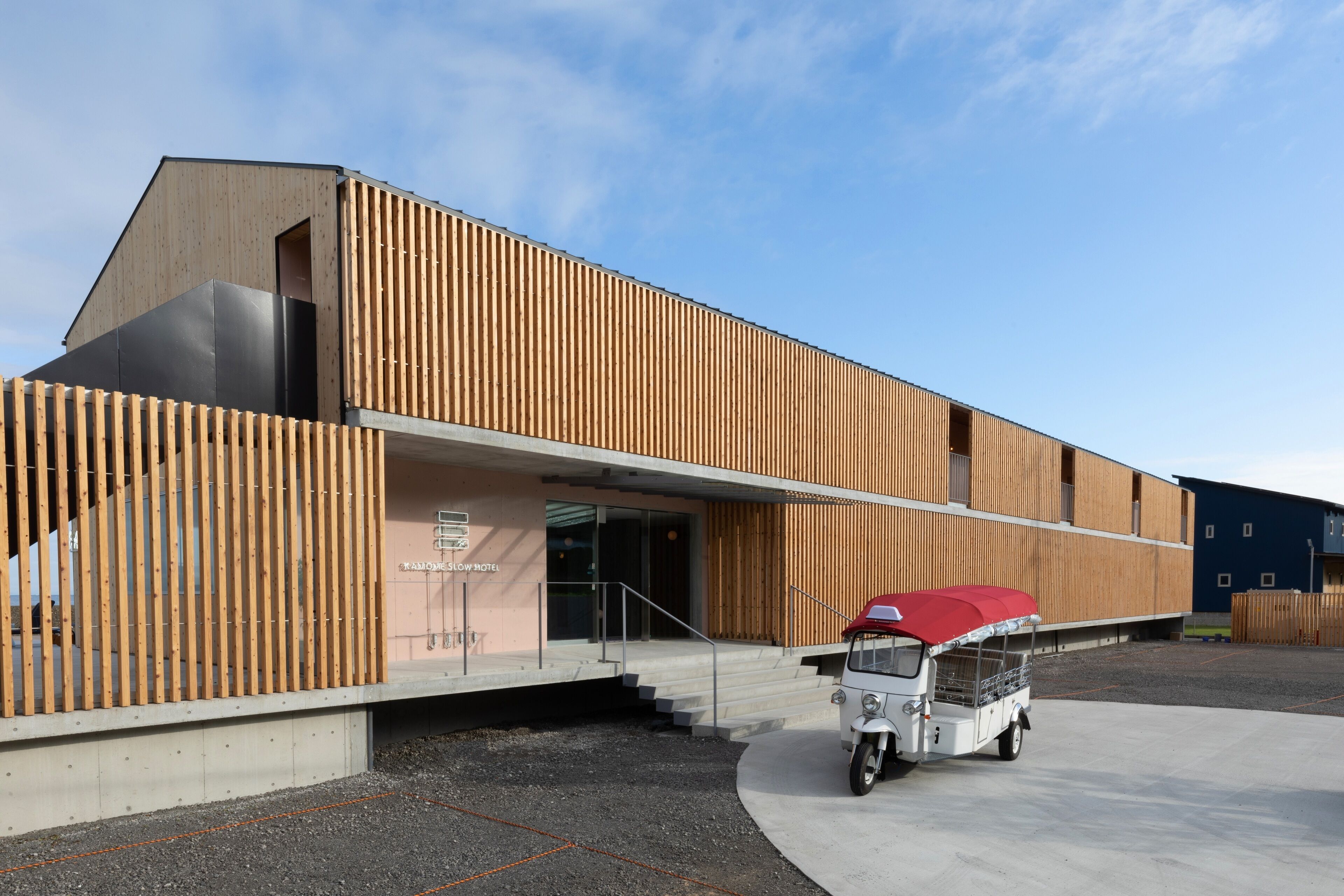 A modern building with a sloped roof, a wooden facade, and a small white truck parked in front.