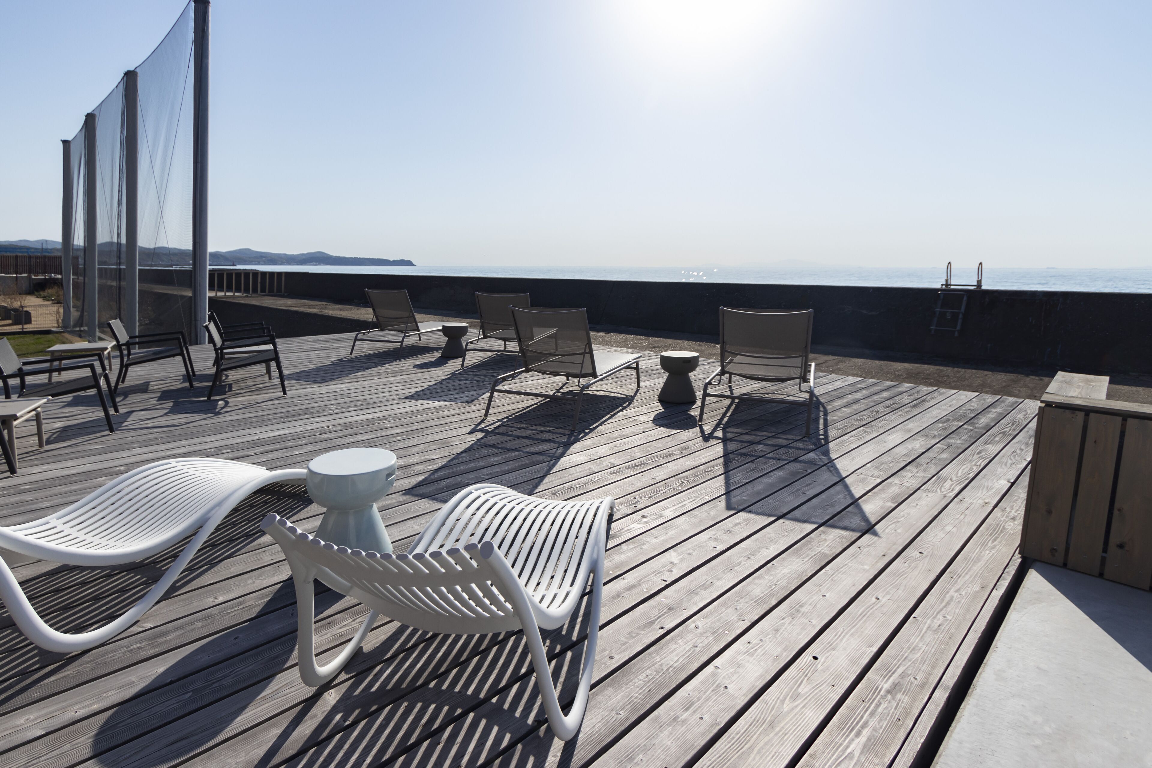 Une terrasse en bois avec des chaises longues blanches et une petite table, donnant sur une étendue d’eau.