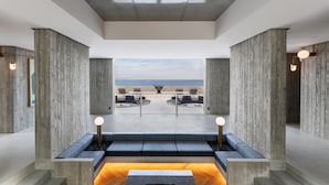 A modern interior with a view of the beach, featuring a seating area with a wooden table and benches, and a large window overlooking the ocean. - Kamome Slow Hotel (Awaji)
