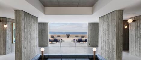 A modern interior with a view of the beach, featuring a seating area with a wooden table and benches, and a large window overlooking the ocean.