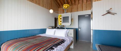 A bedroom with a bed, a vanity with a mirror, and a door.
