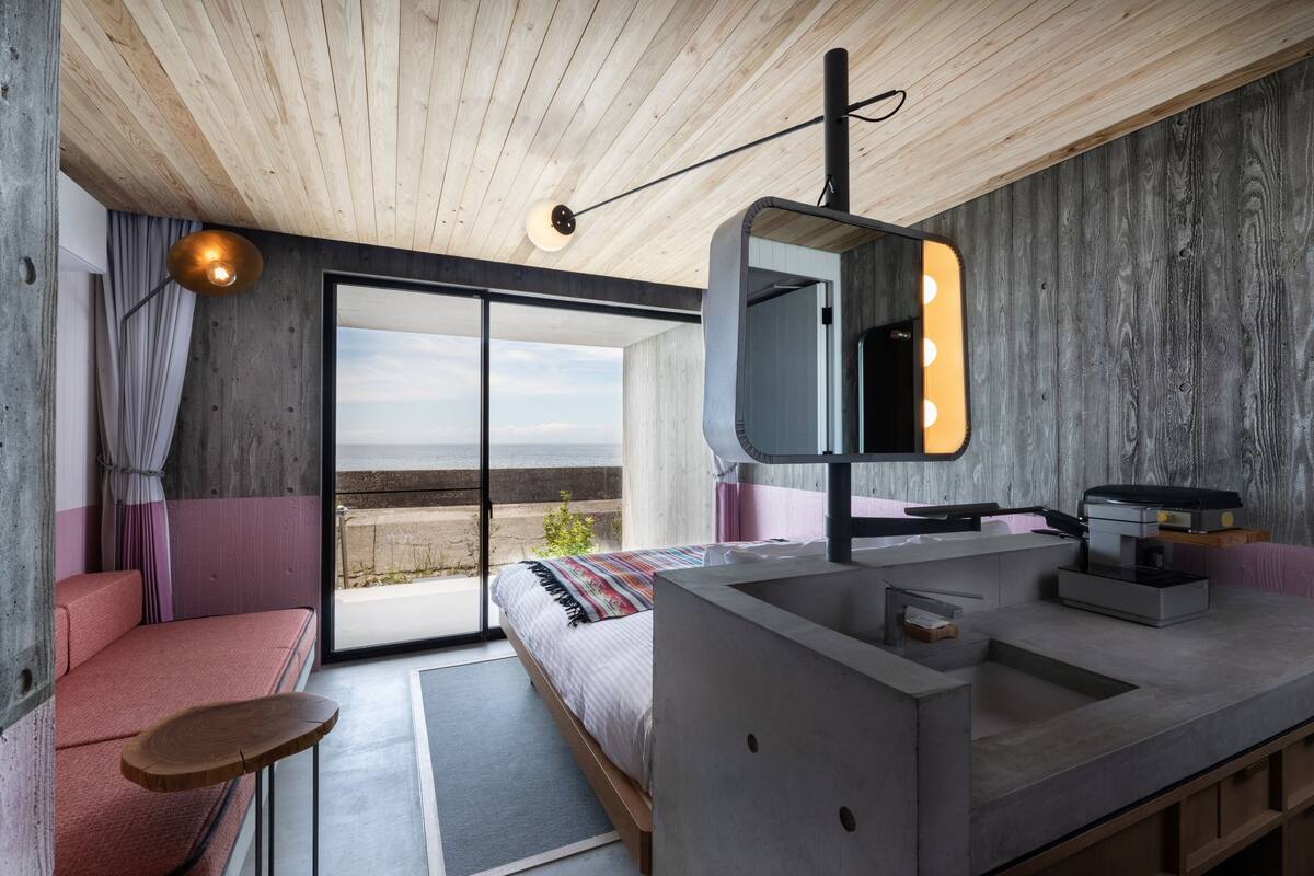 A modern bedroom with a large bed, a vanity with a mirror, a wooden ceiling, and a view of the outdoors.