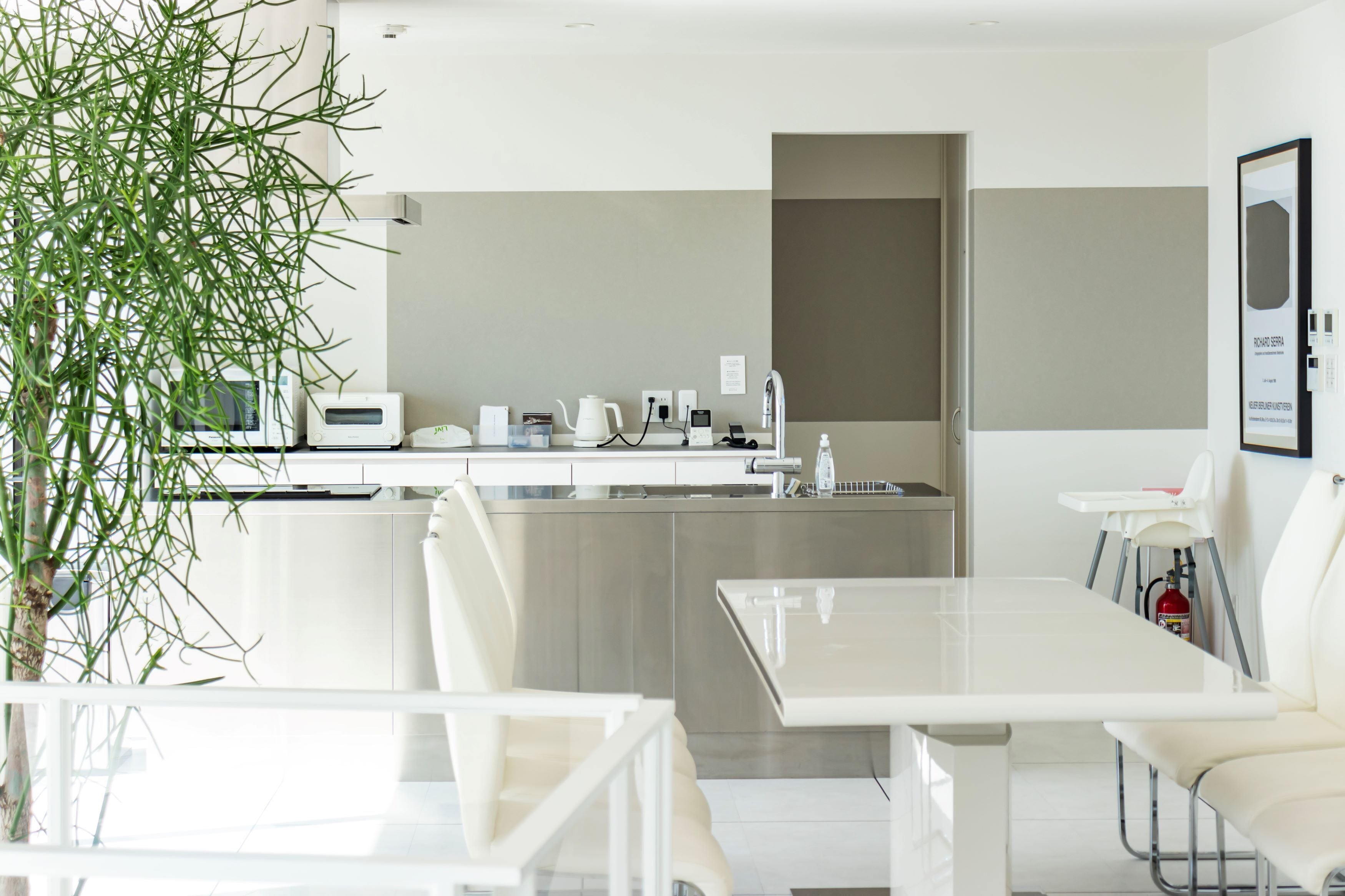 A modern kitchen with white appliances, a dining area with a white table and chairs, and a potted plant.