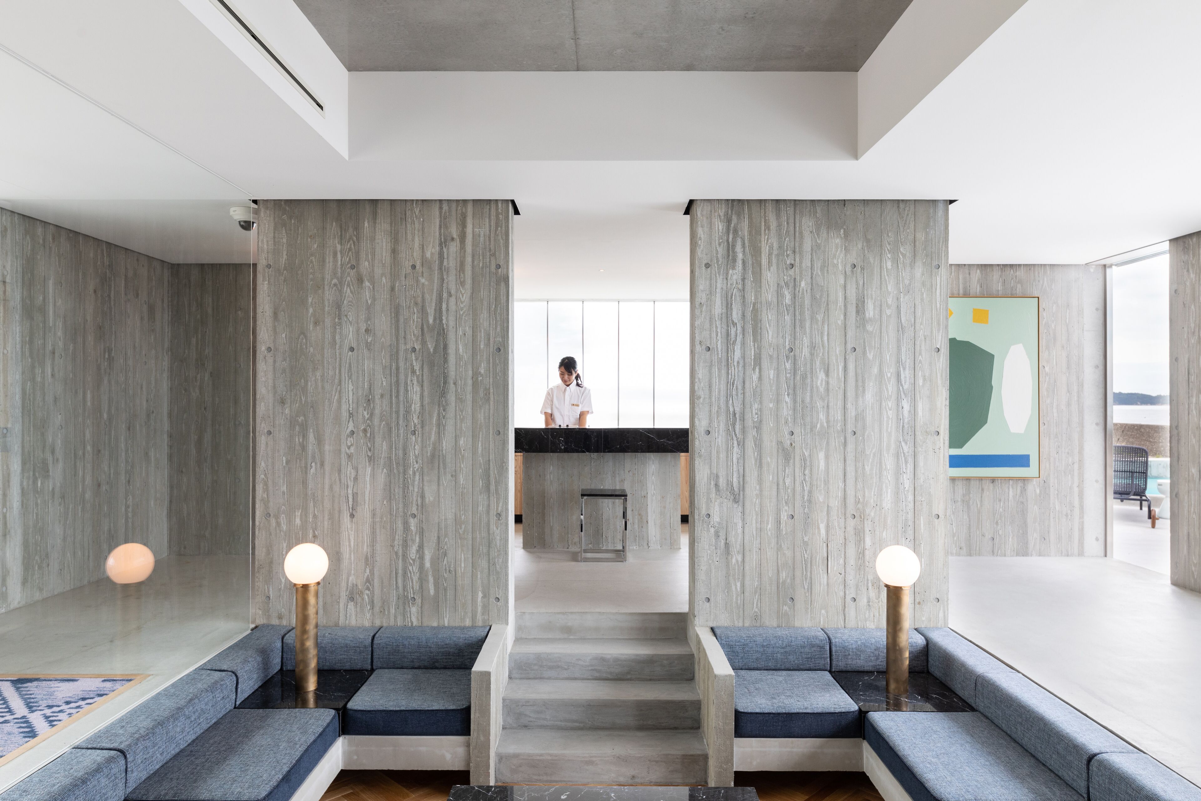 A modern lobby with a central staircase, grey walls, and seating areas with round lights.