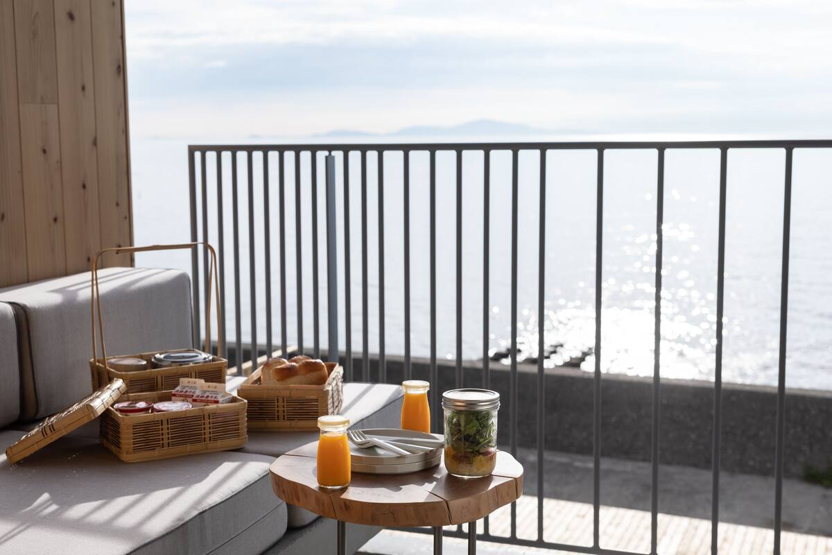 A balcony with a view of the sea, a wooden table with breakfast items, and a wicker basket.