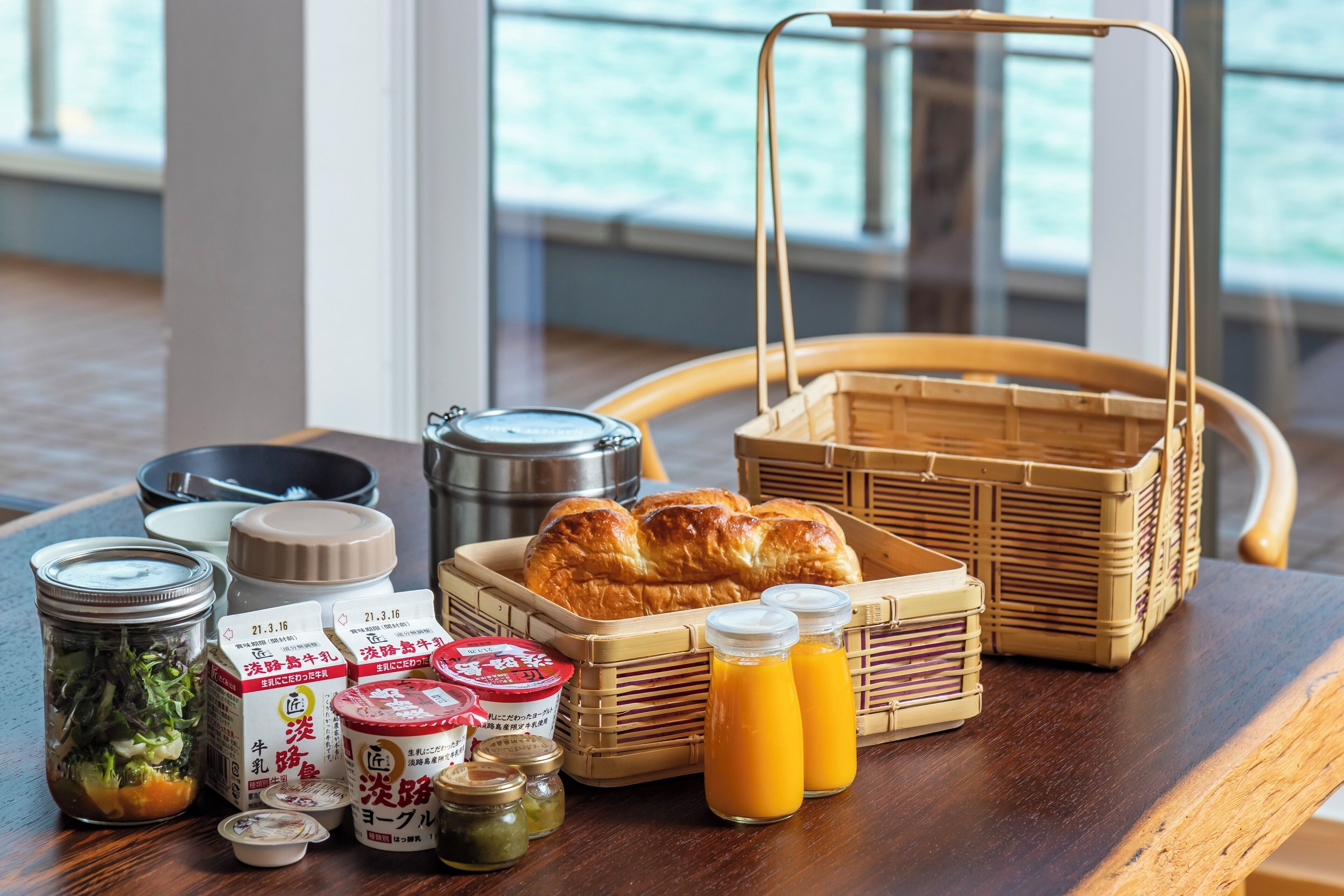 Une table en bois dressée pour le petit-déjeuner, avec du pain, des condiments et des boissons.