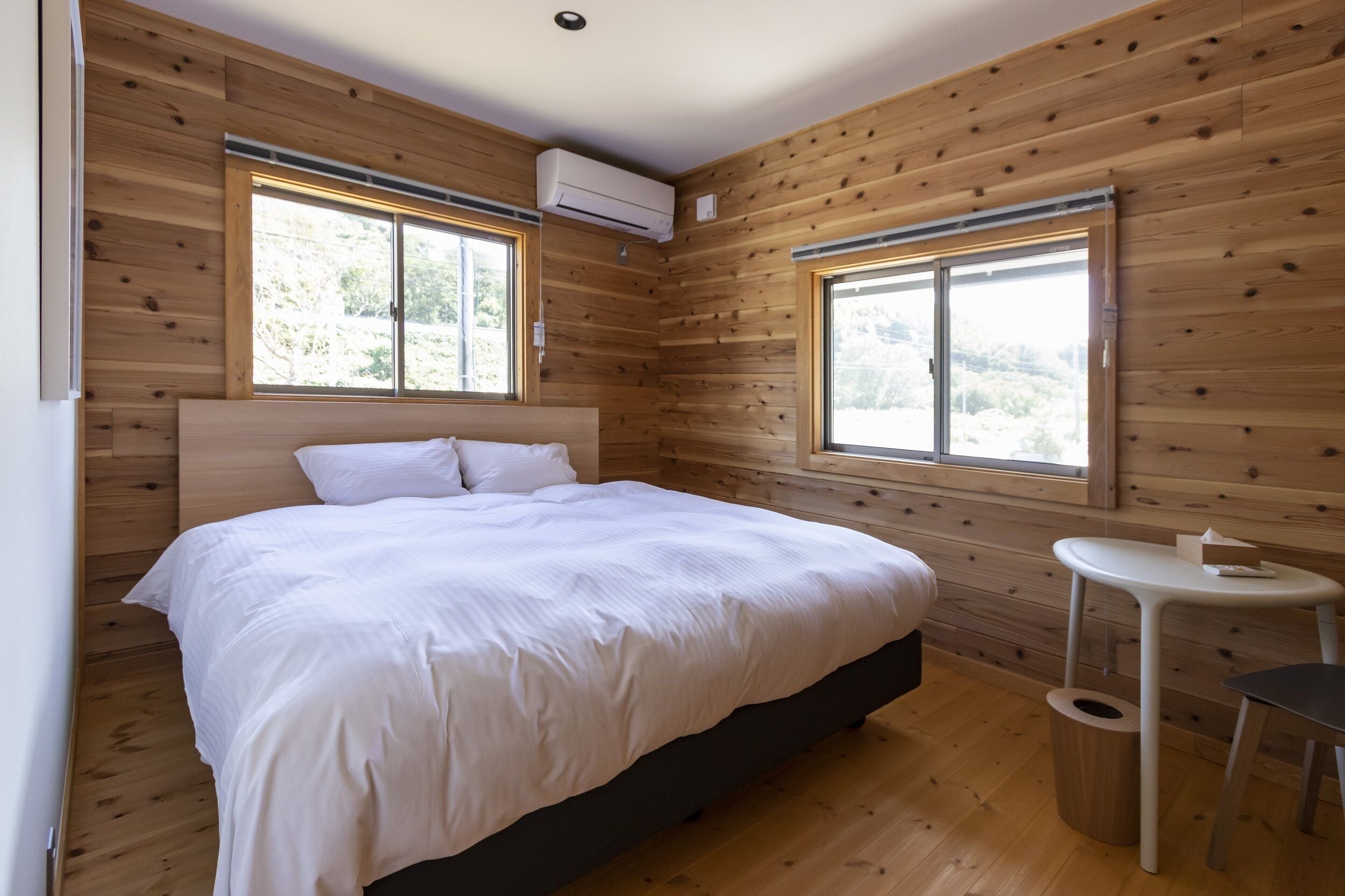 A bedroom with a large bed, wooden walls, and two windows.