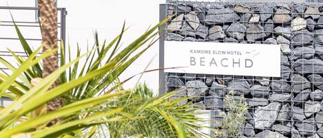 Une enseigne pour le Kamome Slow Hotel Beachd, avec un mur de pierres en arrière-plan et une végétation tropicale au premier plan.