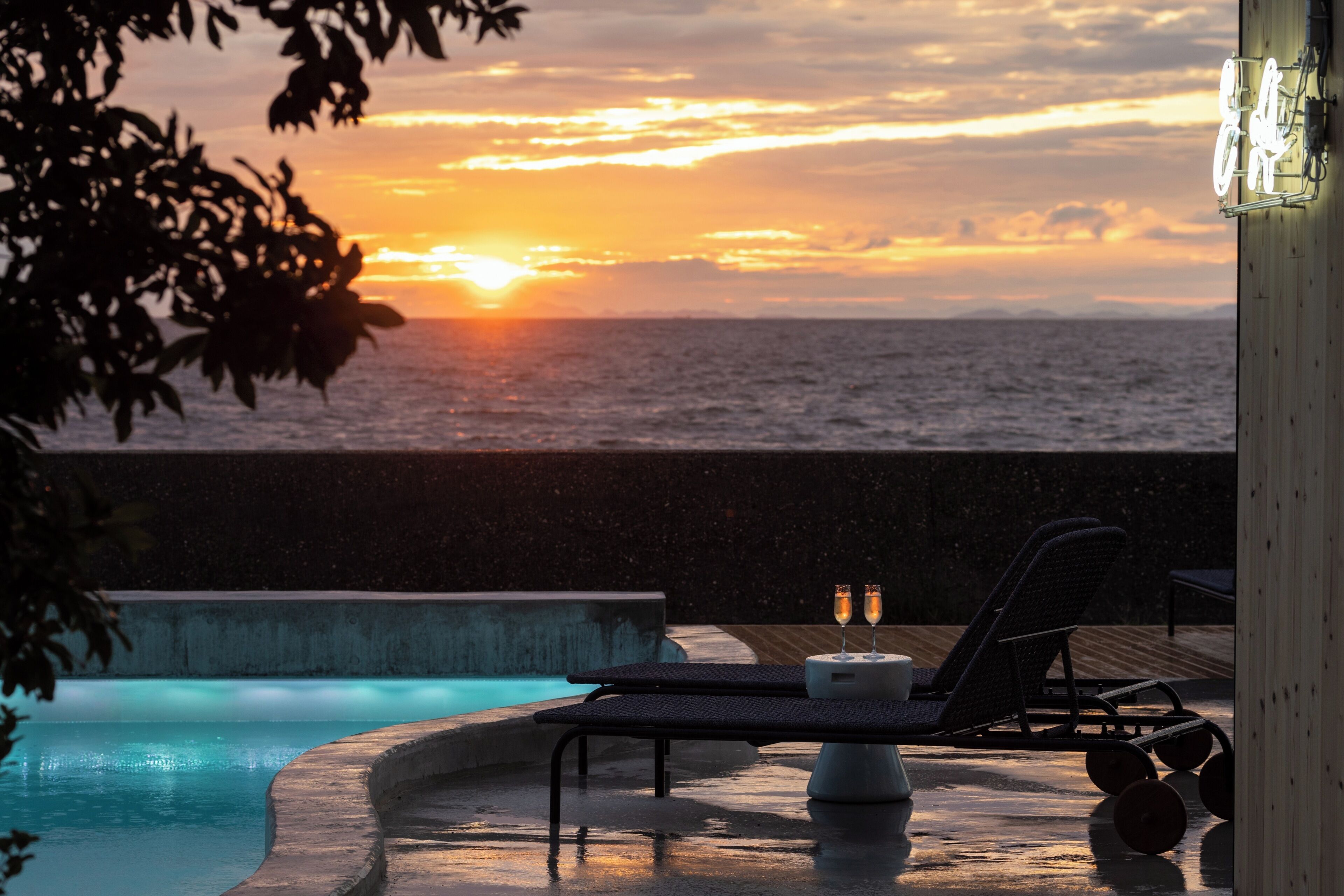 Ein Poolbereich mit Liegestühlen und einem Tisch, mit Blick auf ein Gewässer bei Sonnenuntergang.