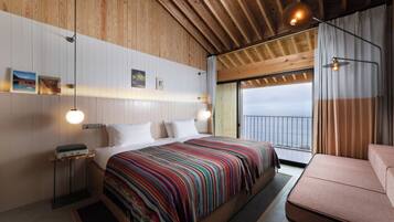 A bedroom with a large bed, a view of the sea, and wooden ceiling beams.