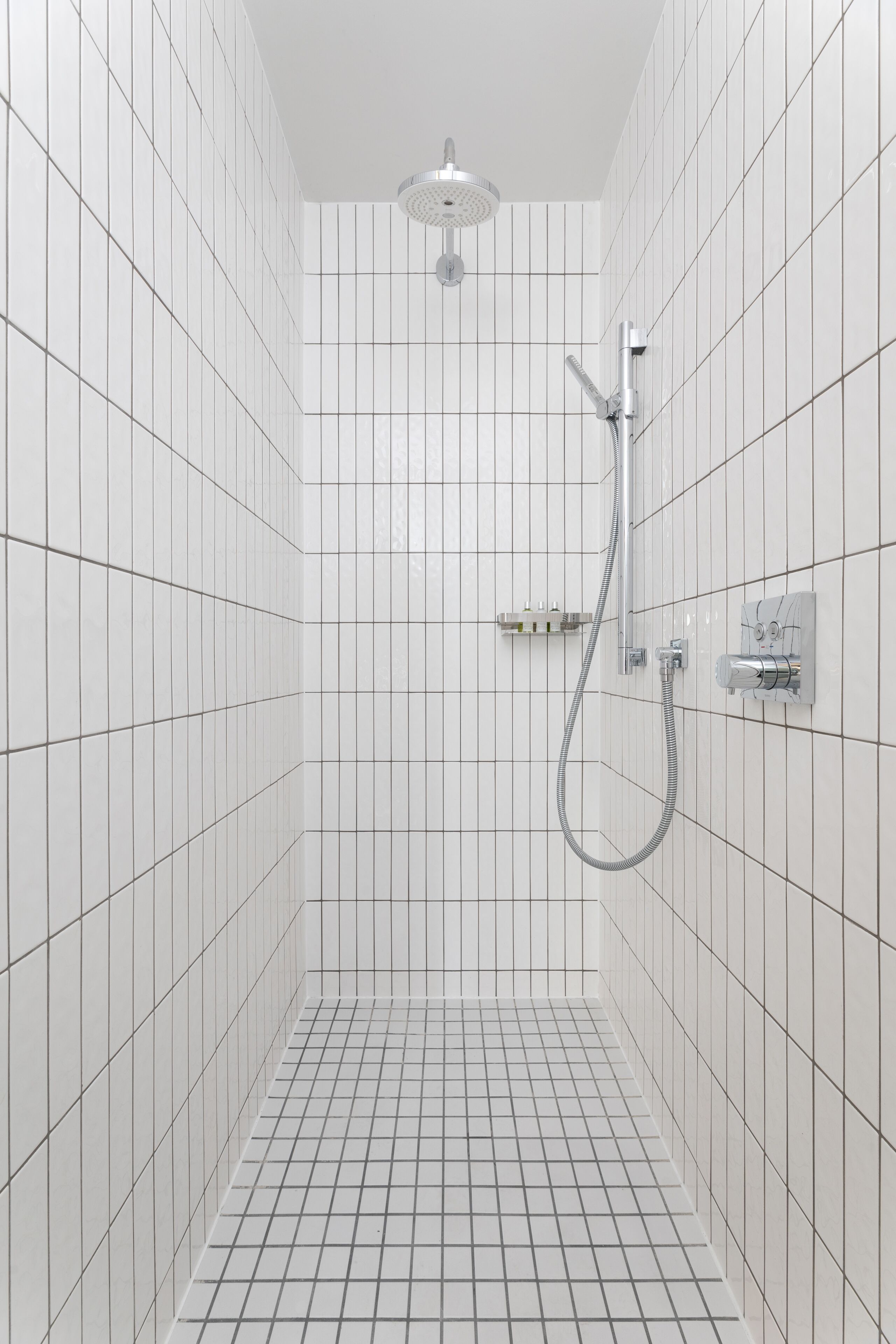A small, tiled shower room with a handheld showerhead and a wall-mounted faucet.