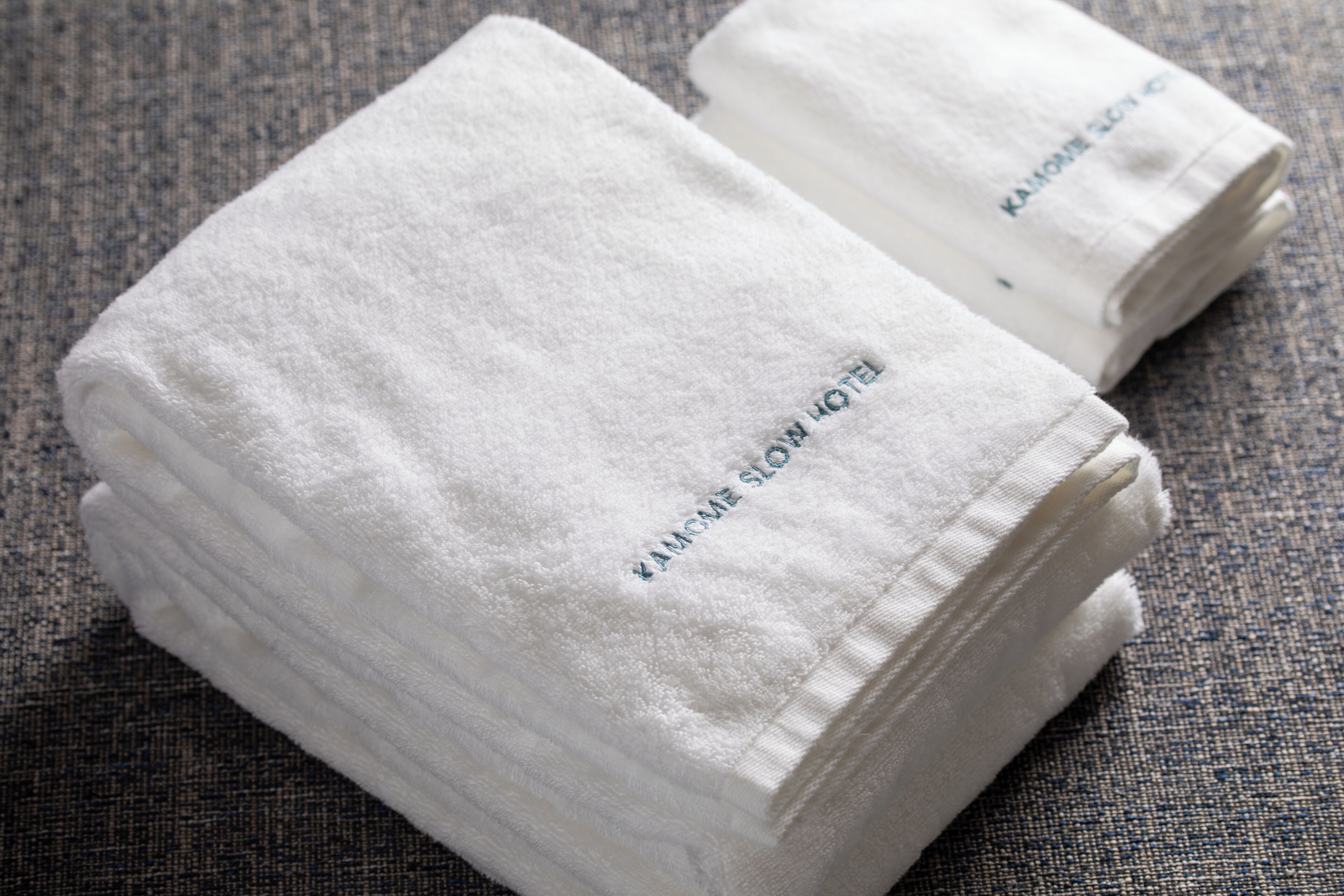 Two neatly folded white towels with embroidered text, placed on a textured fabric surface.