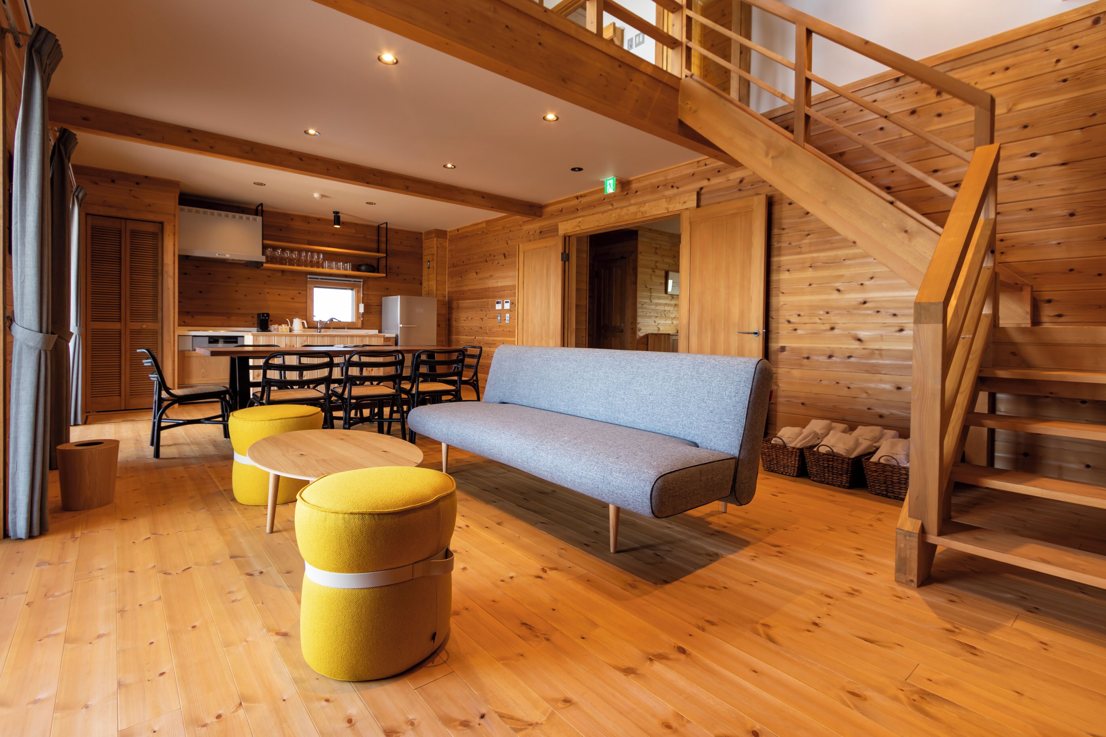 Un intérieur en bois comprenant un canapé, des poufs, un escalier et un coin cuisine.