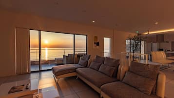 Una sala moderna con un amplio sofá modular, un comedor y vistas al atardecer sobre el agua.
