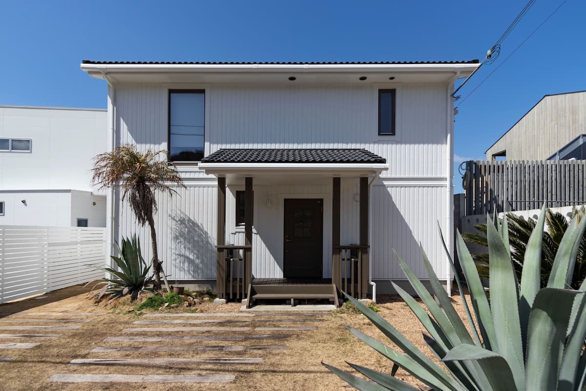 A two-story house with a front porch, a tiled roof, and a wooden fence.