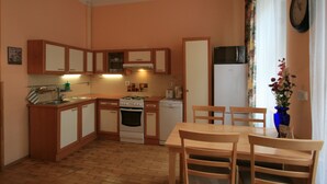 A compact kitchen with wooden cabinets, a microwave, a stove, and a sink. There is a dining table with chairs and a vase with flowers on the table. - Apartment No. 22 Zeyerova 15 (Karlovy Vary)