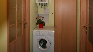 A laundry room with a washing machine, a red flower pot, and a cabinet with a metal container on top. - Apartment No. 22 Zeyerova 15 (Karlovy Vary)