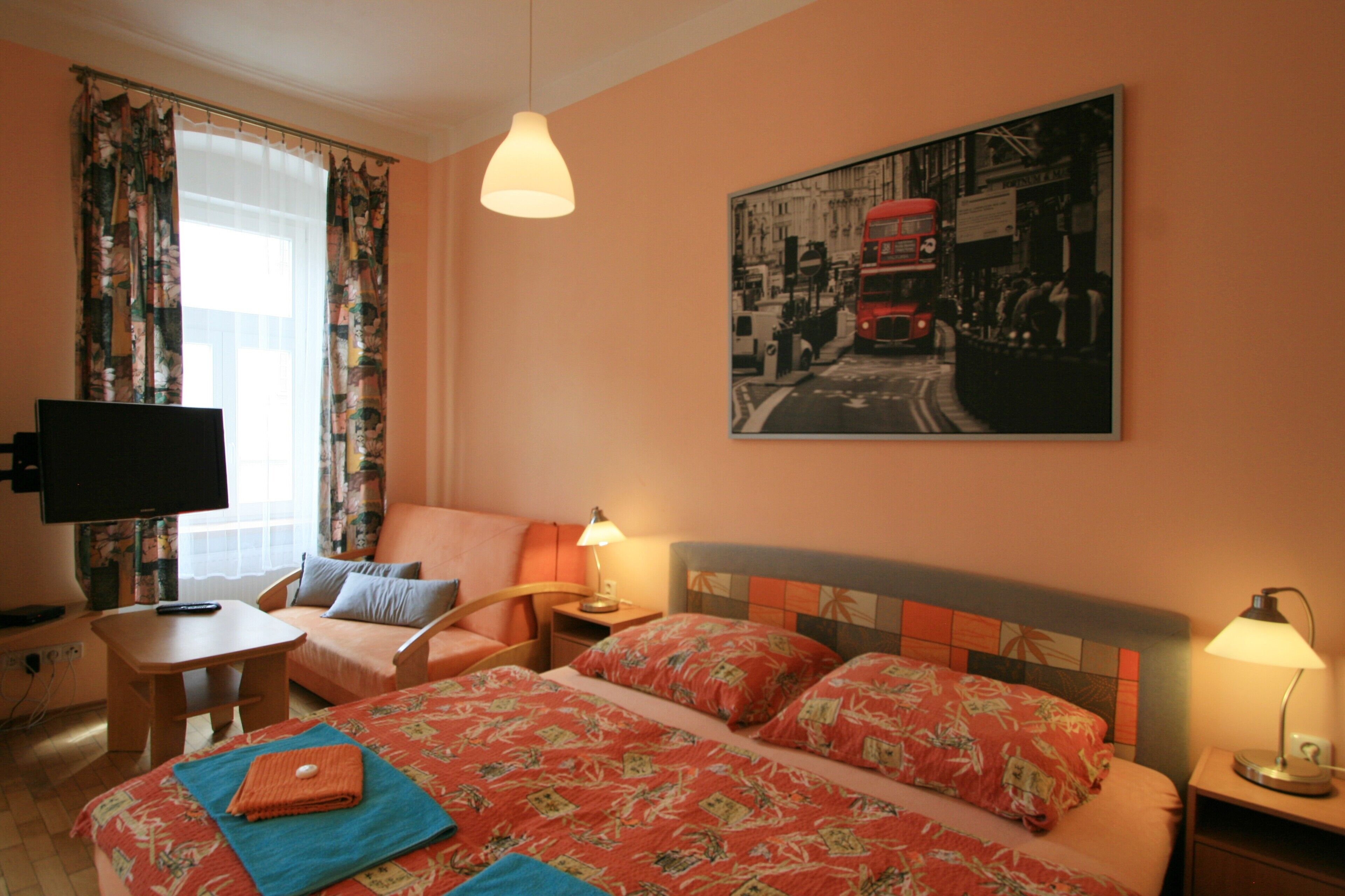A hotel room with a bed, a chair, a small table, a TV, and a painting on the wall.
