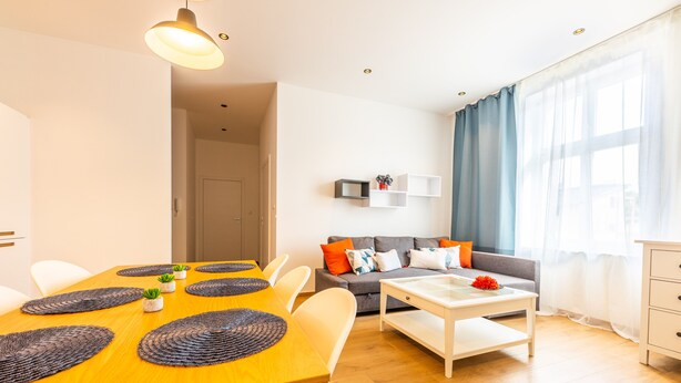 A modern living room with a dining table, sofa, and a TV mounted on the wall. - Victus Apartamenty - Malmo (Sopot)