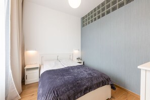 A bedroom with a bed, nightstands, a bedside table, a window with blinds, and a wall with a textured pattern.