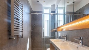 A modern bathroom with a glass shower enclosure, wooden flooring, and a large mirror above the sink. - Victus Apartamenty - Malmo (Sopot)