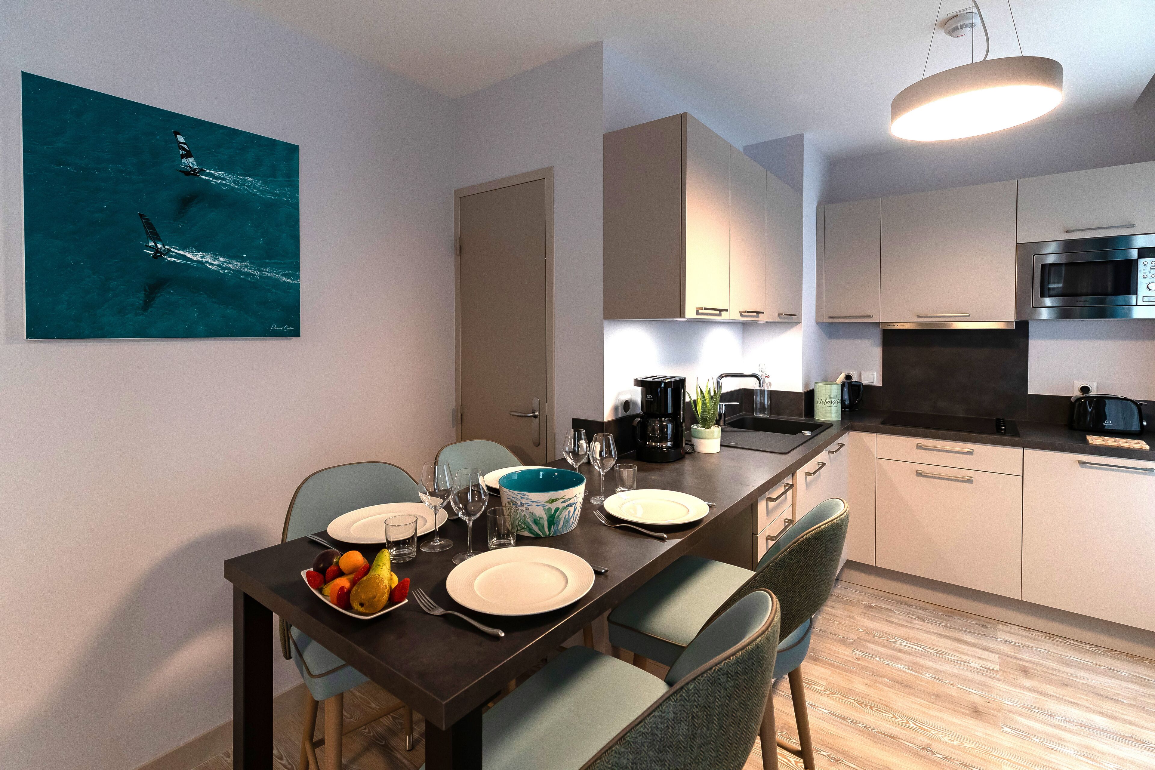 Una cocina moderna con comedor, que incluye una isla grande, armarios blancos y una lámpara colgante.