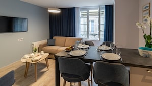 A modern living room with a sofa, a dining table set for two, and a TV mounted on the wall. - Appartement des Marins (Saint-Malo)