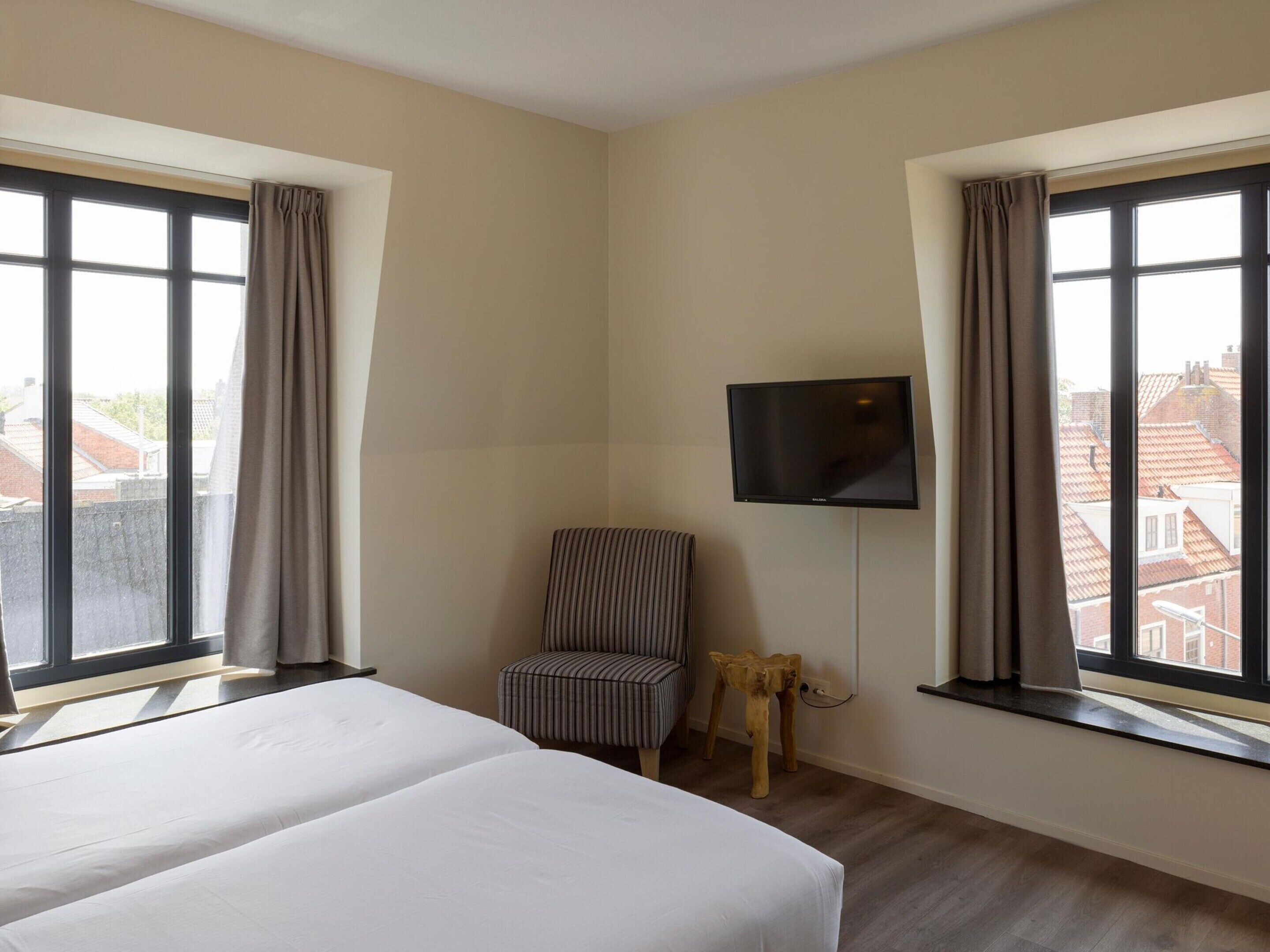Ein Hotelzimmer mit zwei Betten, einem an der Wand befestigten Fernseher und Blick auf Gebäude.