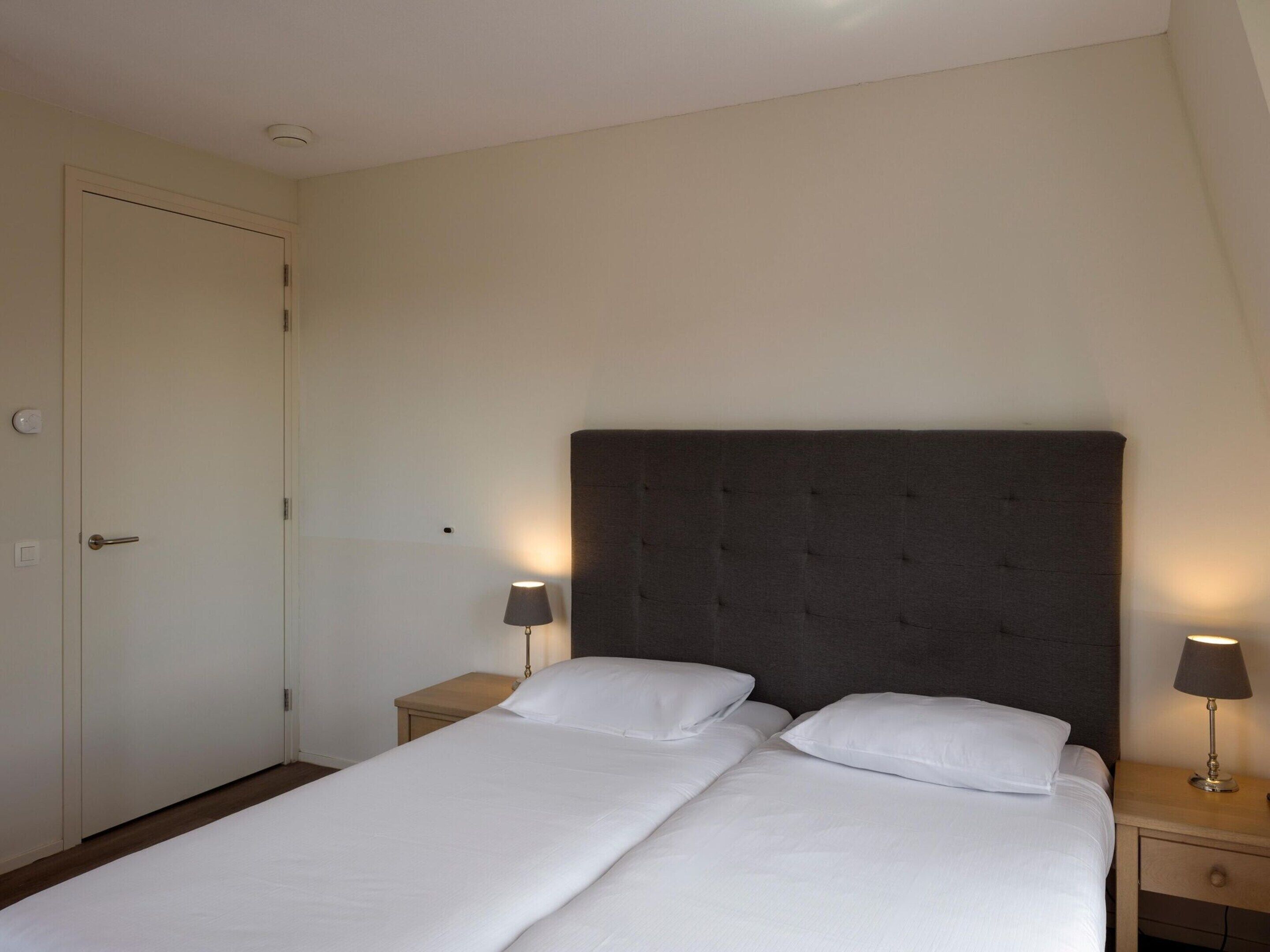 A bedroom with a double bed, two bedside tables, and a door.