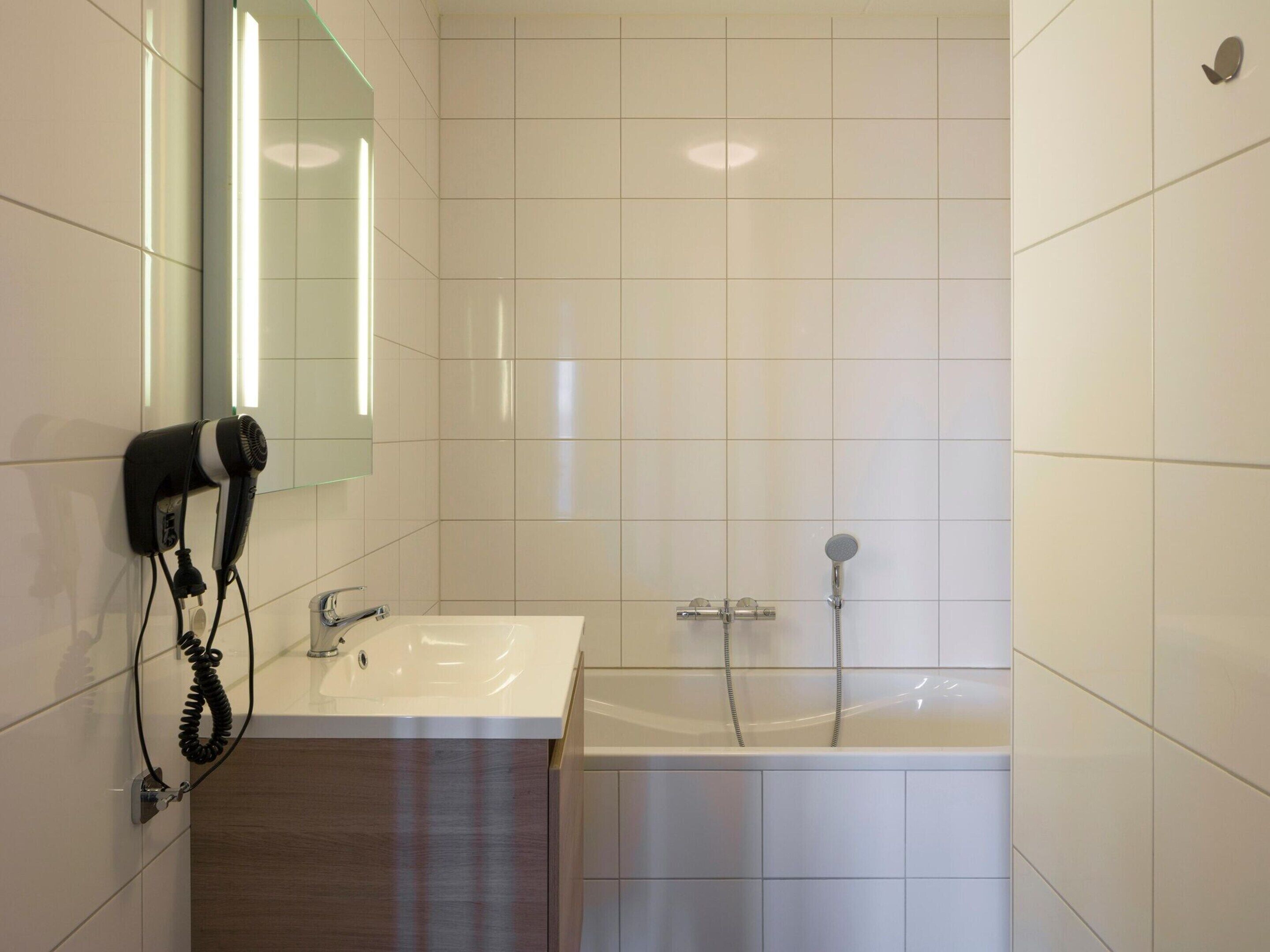 Casa de banho moderna com lavatório branco, espelho, secador de cabelo e banheira.