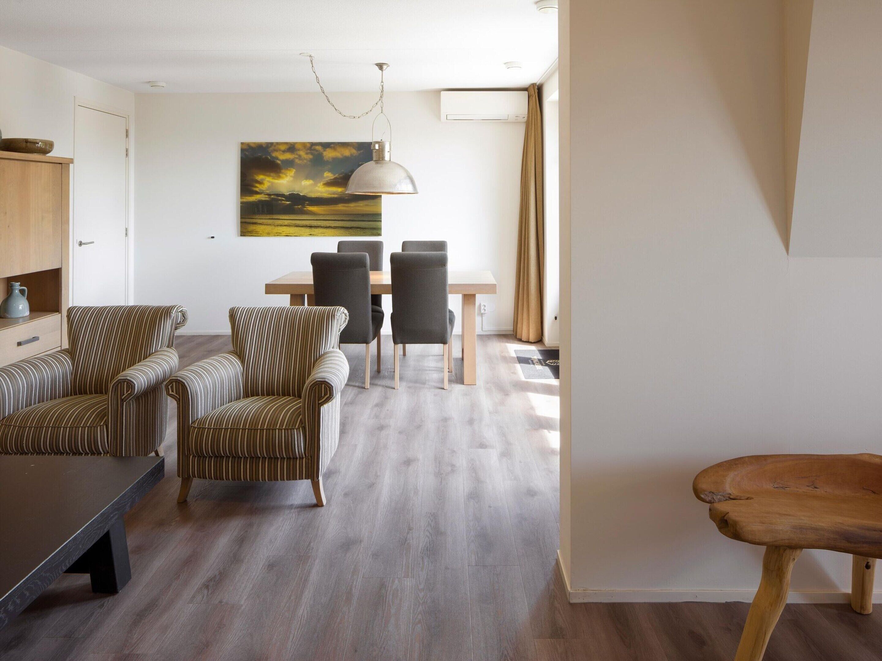 A modern living room with striped sofas, a wooden dining table, and a hanging pendant light.