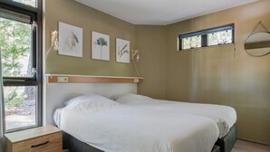 A bedroom with a bed, a bedside table, a window, and wall-mounted artwork. - Woodland Bungalow w/ Pool (Epe)