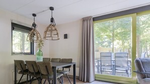 A modern dining area with a table and chairs, large windows with curtains, and hanging pendant lights. - Woodland Bungalow w/ Pool (Epe)