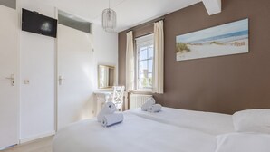 Ein Hotelzimmer mit zwei Betten, einem Schreibtisch, einem Stuhl, einem Fernseher und einem Strandbild.