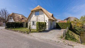 Ein Haus mit Strohdach, befestigter Auffahrt und kleinem Garten.