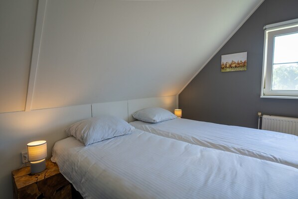 A bedroom with two single beds, a bedside lamp, a radiator, and a picture on the wall. - Wellness Villa by the Weerribben (Paasloo)