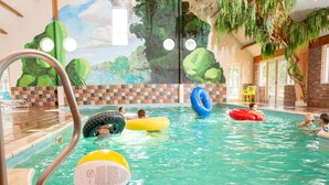 Una piscina interna con acqua cristallina, circondata da un muro rivestito di piastrelle con un affresco raffigurante alberi e da un muro in mattoni.