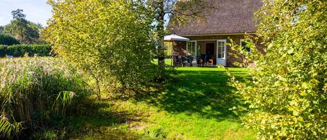 Une maison avec un toit de chaume, une pelouse et un étang.
