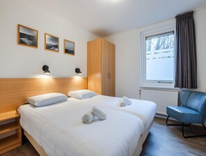 A hotel room with a large bed, two bedside tables, a wooden wardrobe, a window with curtains, and three framed pictures on the wall. - Comfortable Bungalow With Dishwasher Near the Beach (Hollum)