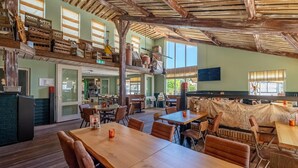 A spacious dining area with wooden tables and chairs, a high ceiling with exposed beams, and a view of the outdoor seating area. - Comfortable Bungalow With Dishwasher Near the Beach (Hollum)