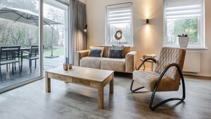 A modern living room with a sofa, a rocking chair, a coffee table, and a dining area with chairs. - Comfortable Bungalow With Dishwasher Near the Beach (Hollum)