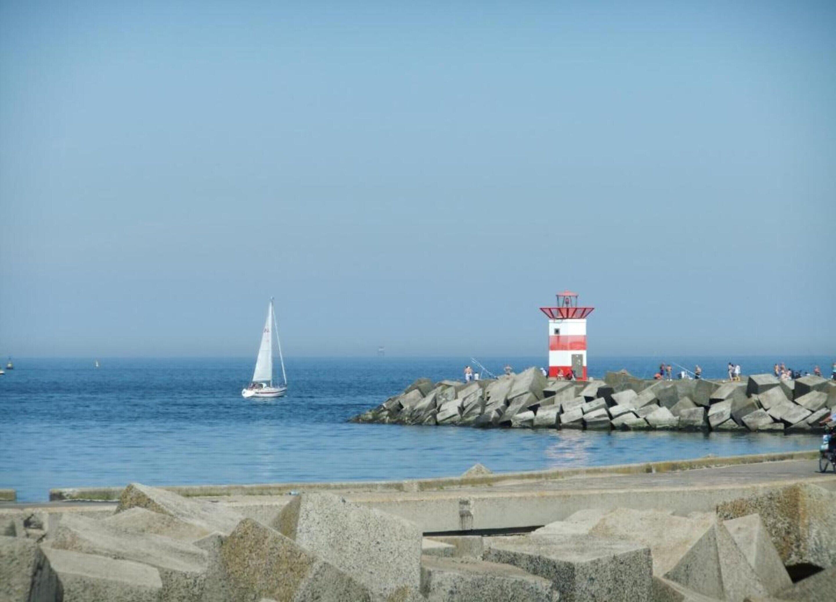 A lighthouse on a rocky pier with a sailboat in the background.