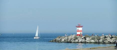 A lighthouse on a rocky pier with a sailboat in the background.