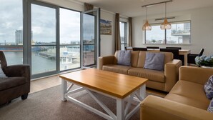 A modern living room with large windows, a sofa, a coffee table, and a dining area. - Modern Apartment 500 m From the Centre of Scheveningen (The Hague)