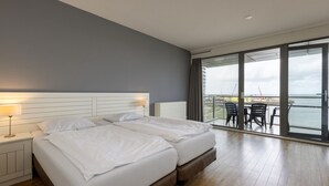 A modern hotel room with a large bed, a balcony with a view of the sea, and a dining area with chairs. - Modern Apartment 500 m From the Centre of Scheveningen (The Hague)