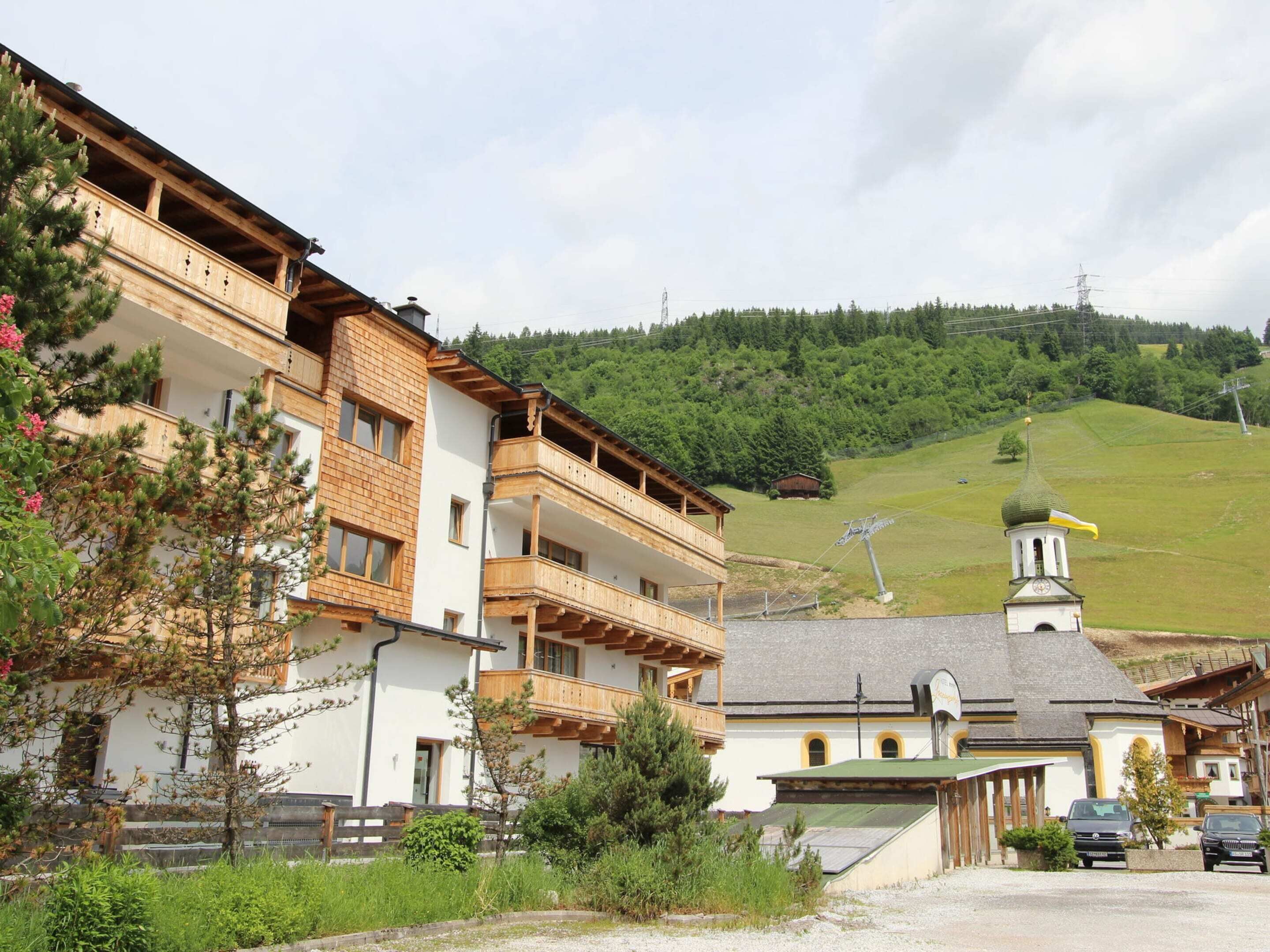 A multi-story building with wooden balconies, a church with a green dome, and a hilly landscape in the background.