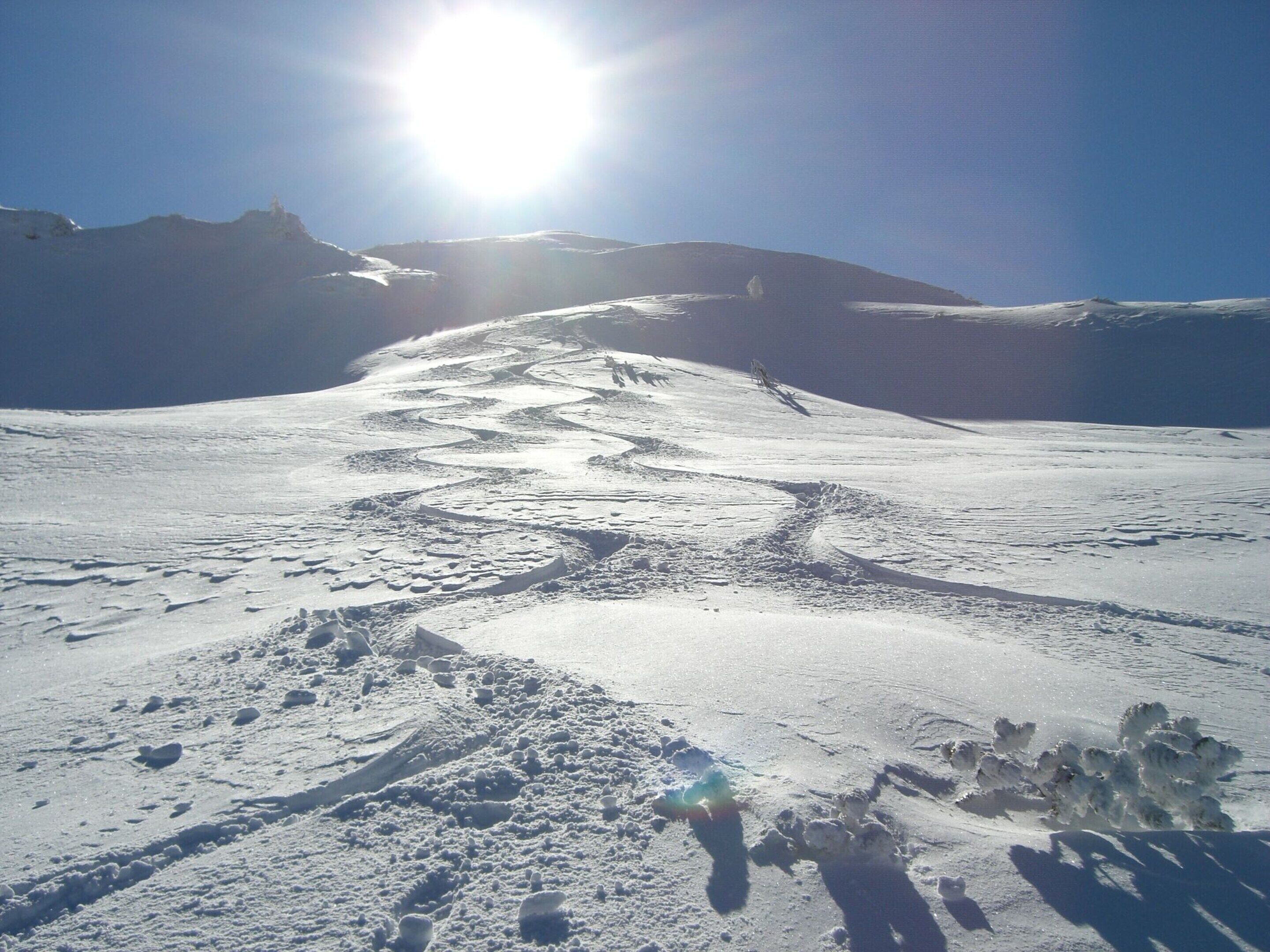 A snow-covered mountain path with a clear sky and the sun shining.