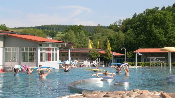 Une piscine où des personnes font de l’exercice, entourée d’immeubles et d’arbres.