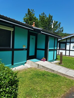 A single-story building with a teal exterior and black trim, featuring a small porch with a bench and a flower arrangement. - Holiday Home in Germany With Scenic Nature (Ronshausen)