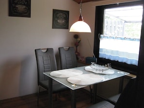 A dining area with a table, chairs, a hanging light fixture, and a window with a view.